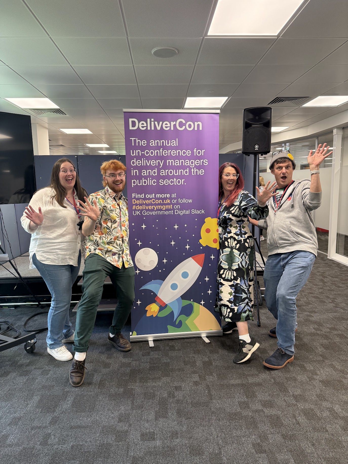 Four people standing in frount of a DeliverCon Banner